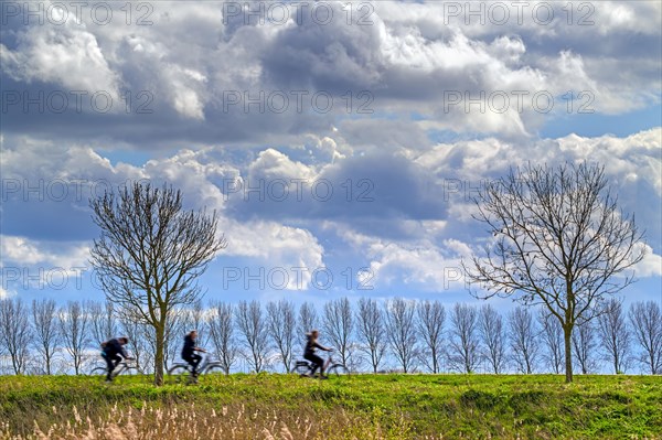 Three cyclists cycling on their bikes under a cloudy sky with cumulus mediocris clouds in early spring