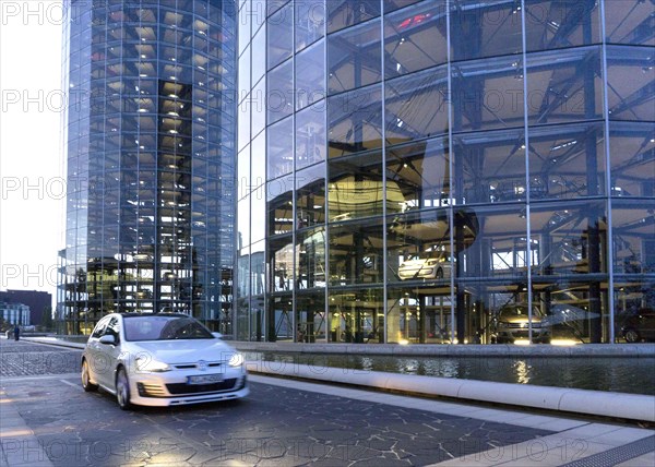 A VW Golf drives past the car towers of the Autostadt, 25 October 2015, Wolfsburg, Lower Saxony, Germany, Europe