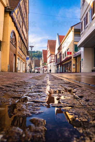 Street view of a European village with traditional half-timbered houses and a puddle reflecting the blue sky, spring, Calw, Black Forest, Germany, Europe