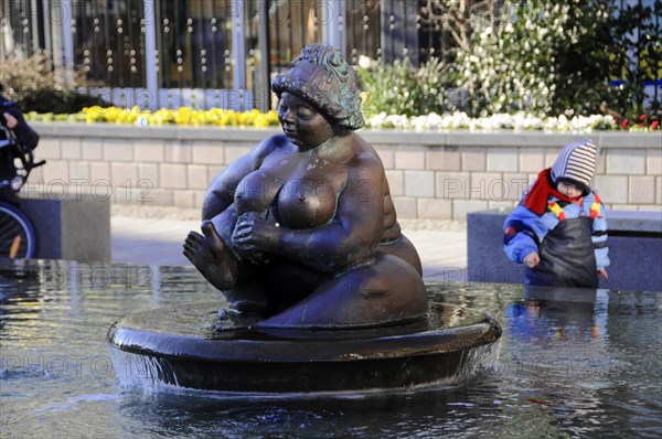 Fountain figure Wilhelmine, landmark of Westerland, Westerland, bronze sculpture of a seated woman in a fountain, a child playing in the background, Sylt, North Frisian Island, Schleswig Holstein, Germany, Europe