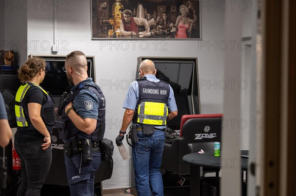 Financial control officers discuss in an office next to a painting, The Cologne police led a raid against illegal gambling on Friday evening. Around 200 investigators from the police, customs, tax investigation, public order office, finance control office, immigration office and the public catering office are on the streets of Cologne on Friday evening. They search 25 properties where there are indications that illegal gambling is taking place. And they make a find