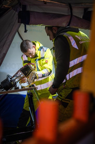 Worker carrying out electrical installation work in an illuminated work tent during the night, Galsfaserbau, Calw, Black Forest, Germany, Europe