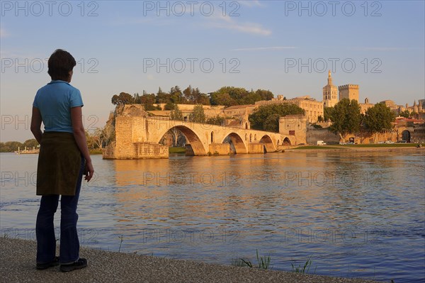Woman on the banks of the Rhone looking towards the Pont Saint Benezet bridge, the Papal Palace and the Cathedral Notre-Dame des Doms, Avignon, Vaucluse, Provence-Alpes-Cote d'Azur, South of France, France, Europe