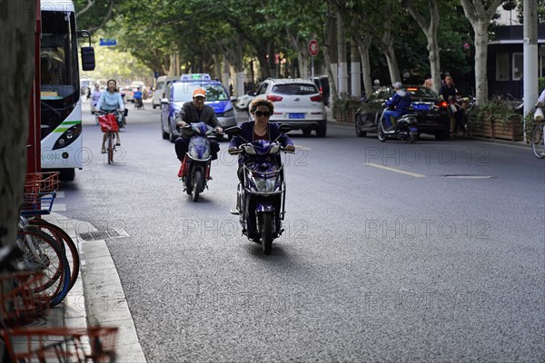 Traffic in Shanghai, Shanghai Shi, people riding scooters and bicycles along a tree-lined street, Shanghai, People's Republic of China