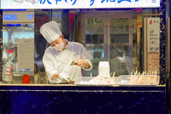 Stroll through Shanghai to the sights, Shanghai, China, Asia, A cook prepares food at a busy street food stall, surrounded by bright lights, Asia