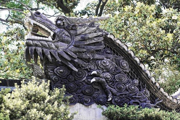 Excursion to the Zhujiajiao water village, Shanghai, China, Asia, An artistic dragon sculpture in stone, embedded in a green bush, symbolises strength, Asia