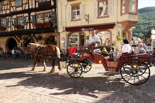 Kaysersberg, Alsace Wine Route, Alsace, Departement Haut-Rhin, France, Europe, A horse-drawn carriage drives through a street with traditional half-timbered houses, Europe
