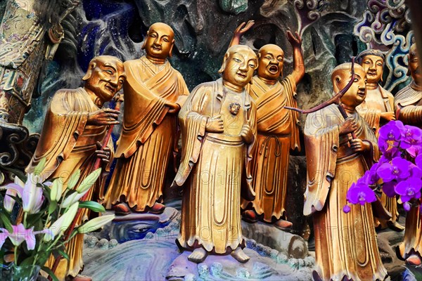 Jade Buddha Temple, Shanghai, Colourful relief of sculptures in traditional robes with purple flowers in the foreground, Shanghai, China, Asia