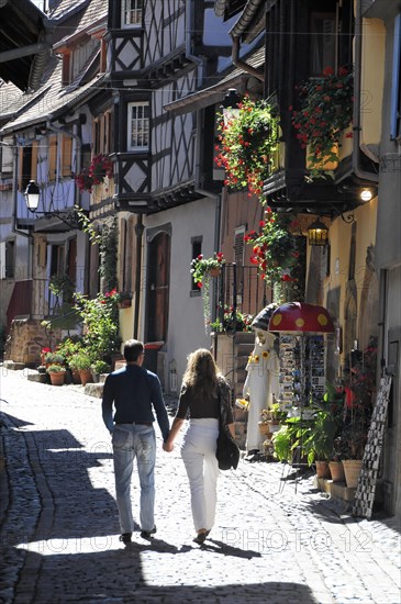 Eguisheim, Alsace, France, Europe, A couple walks hand in hand through a picturesque alley with half-timbered houses, Europe