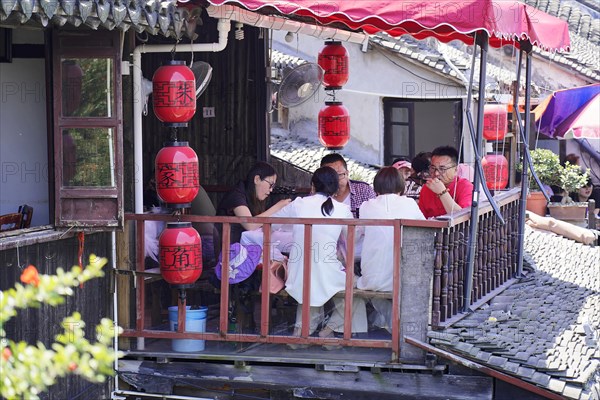 Excursion to Zhujiajiao water village, Shanghai, China, Asia, wooden boat on canal with view of historic architecture, people eating in an outdoor restaurant under red lanterns, Asia