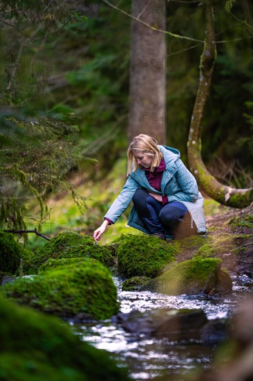 A woman carefully crosses a small, moss-covered stream in the forest, Calw, Black Forest, Germany, Europe
