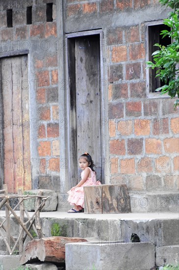 Leon, Nicaragua, A small child sits alone at the entrance of a house with brick walls, Central America, Central America