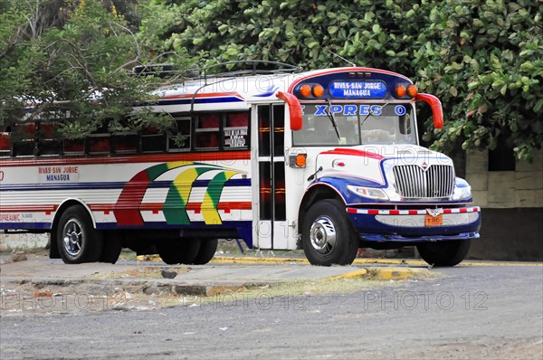 On the road near Rivas, Ometepe Island, Nicaragua, Parked colourful city bus surrounded by trees on a quiet stretch of road, Central America, Central America
