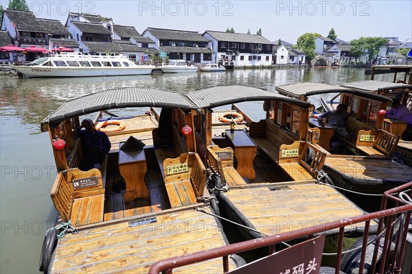 Excursion to Zhujiajiao water village, Shanghai, China, Asia, wooden boat on canal with view of historical architecture, landing stage with passenger boats equipped with roofs on a river, Asia