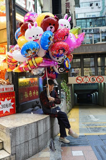 Chongqing, Chongqing Province, China, Asia, A street vendor sits on a wall and sells colourful balloons with caricature figures, Asia