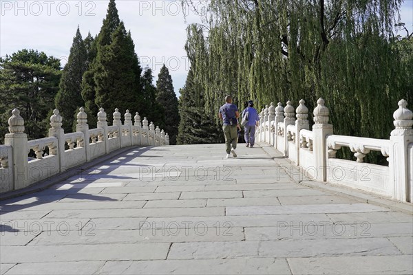New Summer Palace, Beijing, China, Asia, Two people walking across a bridge with white railings next to green trees, Beijing, Asia