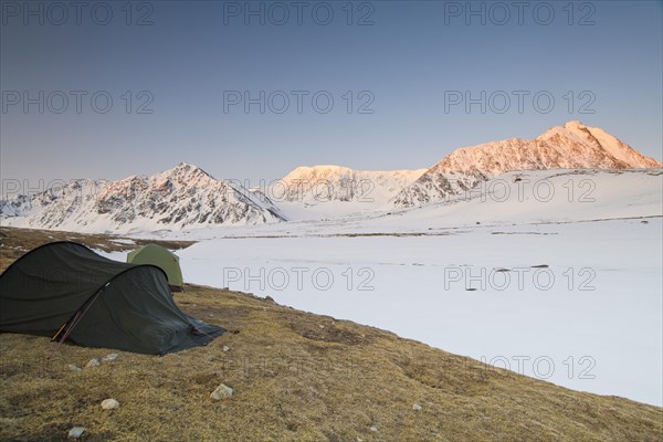Icy tents in expedition camp at sunrise over the mountain peaks in the snow-covered Tavan Bogd National Park, Mongolian Altai Mountains, Western Mongolia, Mongolia, Asia