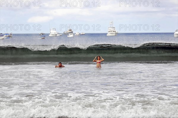 San Juan del Sur, Nicaragua, Swimmers in the sea with a big wave in the background and boats on the horizon, Central America, Central America