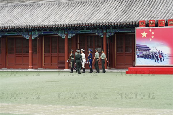 China, Beijing, Forbidden City, UNESCO World Heritage Site, A group in uniforms chatting on the forecourt of a historic building with a red banner, Asia