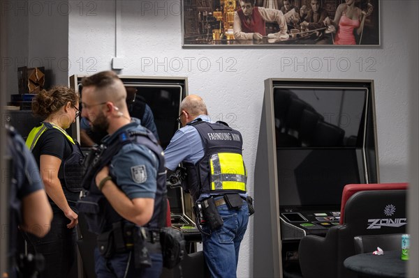 Customs officers talking inside a gaming room with surveillance monitors, The Cologne police led a raid against illegal gambling on Friday evening. Around 200 investigators from the police, customs, tax investigation, public order office, the tax office, the immigration office and the public catering office were out on the streets of Cologne on Friday evening. They search 25 properties where there are indications that illegal gambling is taking place. And they make a find
