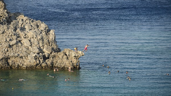 People jumping from cliffs into the sea, surrounded by swimmers in clear water, Lindos, Rhodes, Dodecanese, Greek Islands, Greece, Europe