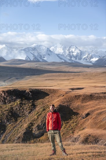 Young man in autumnal mountain landscape with yellow grass in the morning light, glaciated and snow-capped mountains in the background, Tian Shan, Sky Mountains, Sary Jaz Valley, Kyrgyzstan, Asia