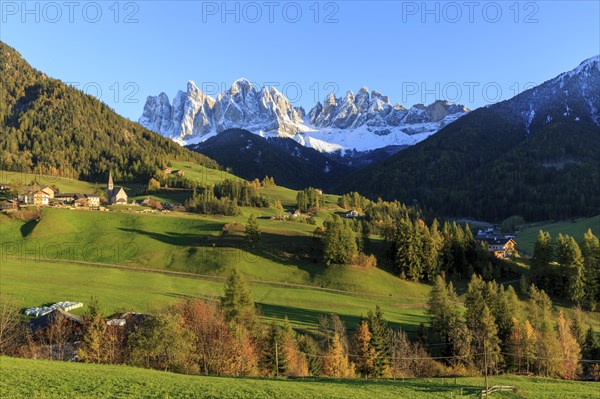 Sunlit village in a valley below a snow-covered mountain range, Italy, Trentino-Alto Adige, Alto Adige, Bolzano province, Dolomites, Santa Magdalena, St. Maddalena, Funes Valley, Odle, Puez-Geisler Nature Park in autumn, Europe