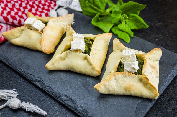 Delicious Lebanese (Arabic) food, spinach sfiha with ricotta cheese on a black slate stone background and traditional Lebanese turban Keffiyeh