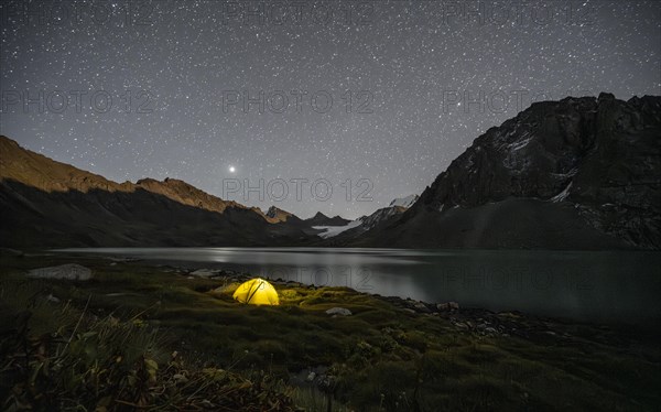 Yellow illuminated camping tent under a starry sky at the mountain lake Ala Kul Lake, mountain landscape at the lake at night, Ala Kul Lake, Tien Shan Mountains, Kyrgyzstan, Asia