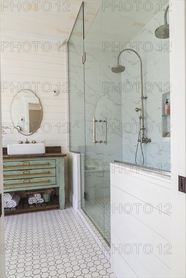 Green antique finish pine wood vanity with rustic wood plank countertop and white top-mounted vessel sink, glass and marble ceramic tile shower stall in en suite with honeycomb ceramic tile flooring on upstairs floor inside country style home, Quebec, Canada, North America