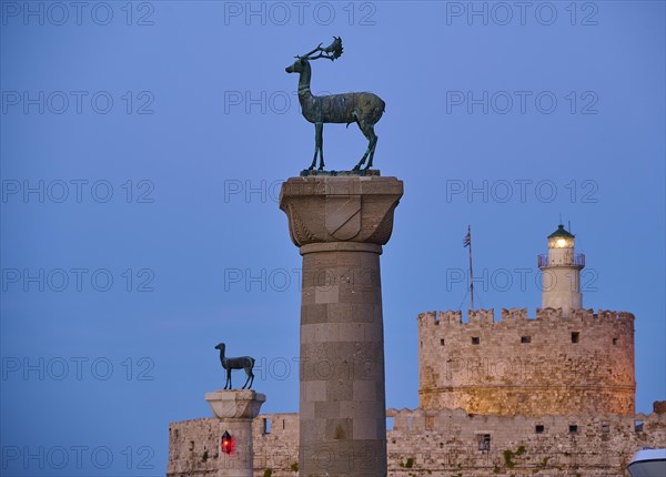 Deer statue on a pillar in front of a fortress wall and a lighthouse at dusk, Deer statue, Deer statue, Fort Agios Nikolaos, Mandraki harbour, European roe deer, Rhodes, Dodecanese, Greek Islands, Greece, Europe
