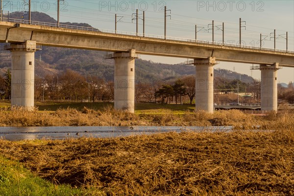 Landscape of railroad bridge running along side river under blue sky in South Korea