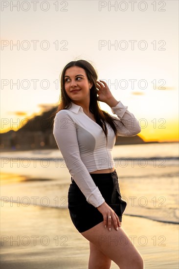 Vertical photo of a distracted chic sensual woman posing on the beach during sunset