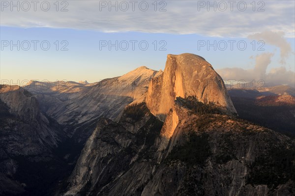 The setting sun bathes Half Dome in orange hues, surrounded by dramatic clouds, Yosemite National Park, North America, USA, South-West, California, California, North America