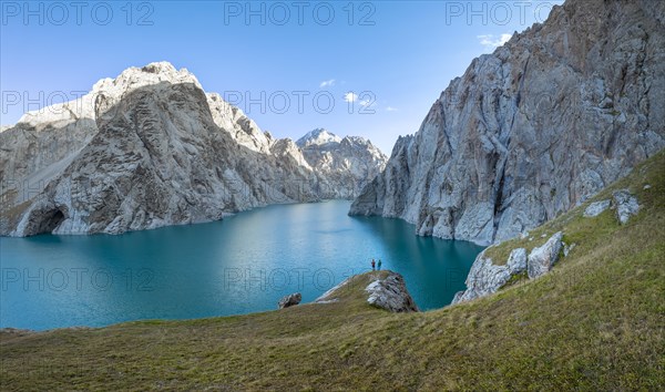 Two hikers, turquoise mountain lake Kol Suu with rocky steep mountains, Kol Suu Lake, Sary Beles Mountains, Naryn Province, Kyrgyzstan, Asia