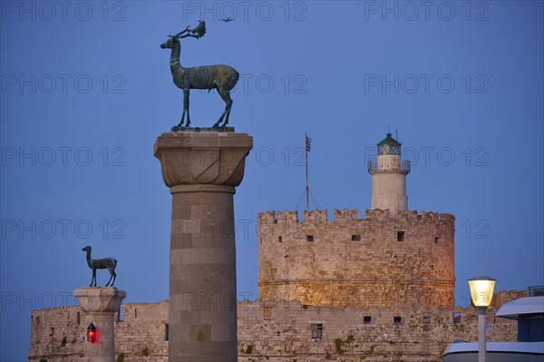 Bronze deer on pedestal in the foreground with old fortress walls and lighthouse in the background, Deer statue, Deer statue, Fort Agios Nikolaos, Mandraki harbour, European roe deer, Rhodes, Dodecanese, Greek Islands, Greece, Europe