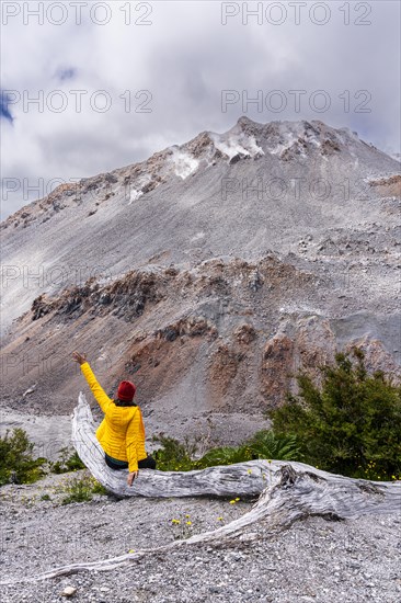 Young woman in yellow jacket sits in front of a volcano, Chaiten Volcano, Carretara Austral, Chile, South America