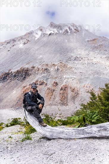 Young man sits in front of a volcano, Chaiten Volcano, Carretara Austral, Chile, South America