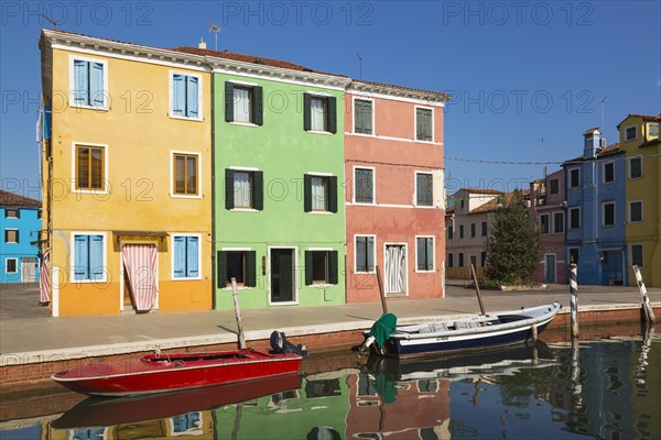 Moored boats on canal lined with orange, green and pink stucco houses decorated with striped curtains over entrance doors, Burano Island, Venetian Lagoon, Venice, Veneto, Italy, Europe