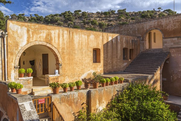 Stone staircase leading to cloister and wall with various plants in terracotta planters in inner courtyard at Holy Trinity (Agia Triada) Monastery, Akrotiri Peninsula, Chania region, Crete Island, Greece, Europe