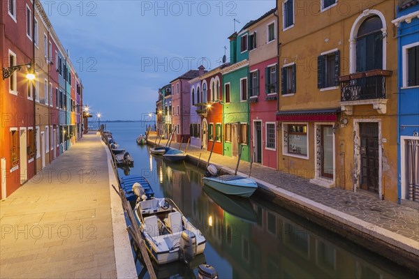 Moored boats on canal lined with colourful stucco houses and storefronts at dusk, Burano Island, Venetian Lagoon, Venice, Veneto, Italy, Europe