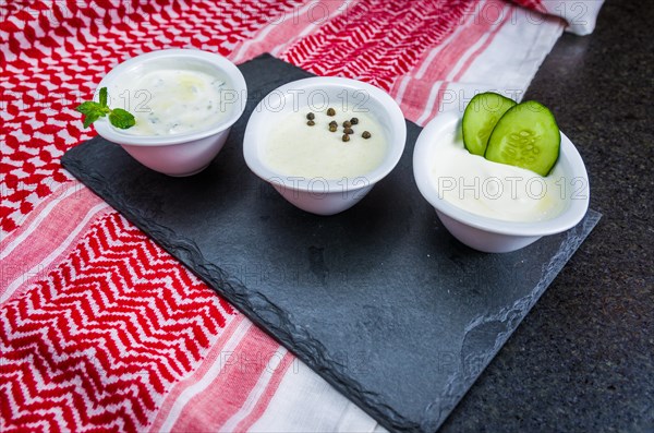 Delicious Lebanese (Arabic) food, thum, labneh and tzatziki sauces on black slate stone background and traditional Lebanese Keffiyeh turban