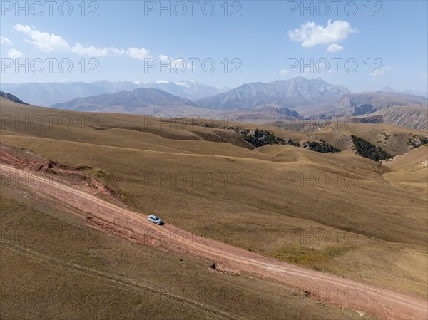 Moldo-Ashuu Pass, car on road between yellow hills, near Baetov, Naryn region, Kyrgyzstan, Asia