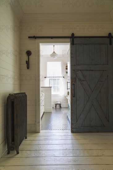 Kid's upstairs floor bathroom with distressed barn wood door, black honeycomb ceramic tile floor, white antique style finish cabinet, freestanding claw foot bathtub inside country style home, Quebec, Canada, North America