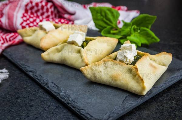 Delicious Lebanese (Arabic) food, spinach sfiha with ricotta cheese on a black slate stone background and traditional Lebanese turban Keffiyeh