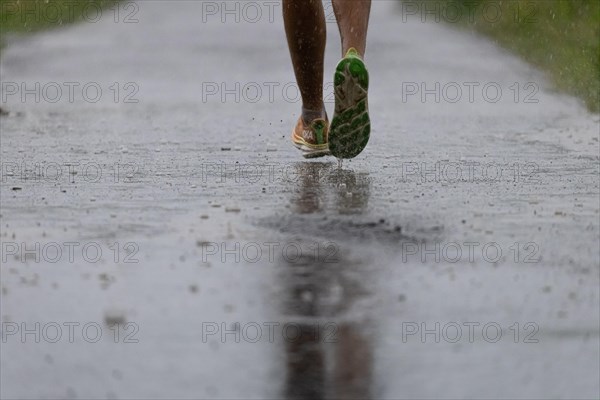 A jogger runs along a dirt track in heavy rain in the north-west of Frankfurt am Main, Frankfurt am Main, Hesse, Germany, Europe
