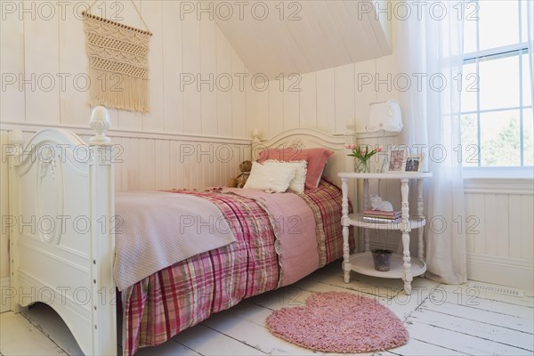 Single bed with red, pink and grey tartan bedspread, white painted antique style wooden headboard and footboard, nightstand in a kid's bedroom with white painted larch wood floorboards on upstairs floor inside country style home, Quebec, Canada, North America