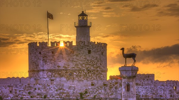 Lighthouse on a castle, pierced by the rays of the rising sun, sunrise, dawn, European roe deer statue, Fort of Saint Nikolaos, harbour promenade, Rhodes, Dodecanese, Greek Islands, Greece, Europe