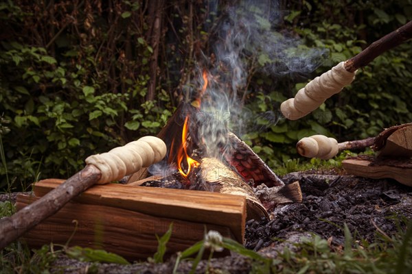 Stick bread is baked over a cosy campfire surrounded by green nature