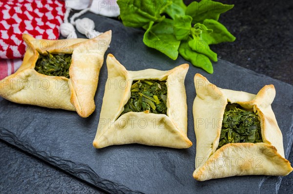 Delicious Lebanese (Arabic) food, spinach sfiha on black slate stone background and traditional Lebanese turban Keffiyeh